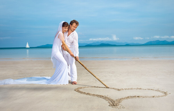 Married couple on the beach drawing a heart